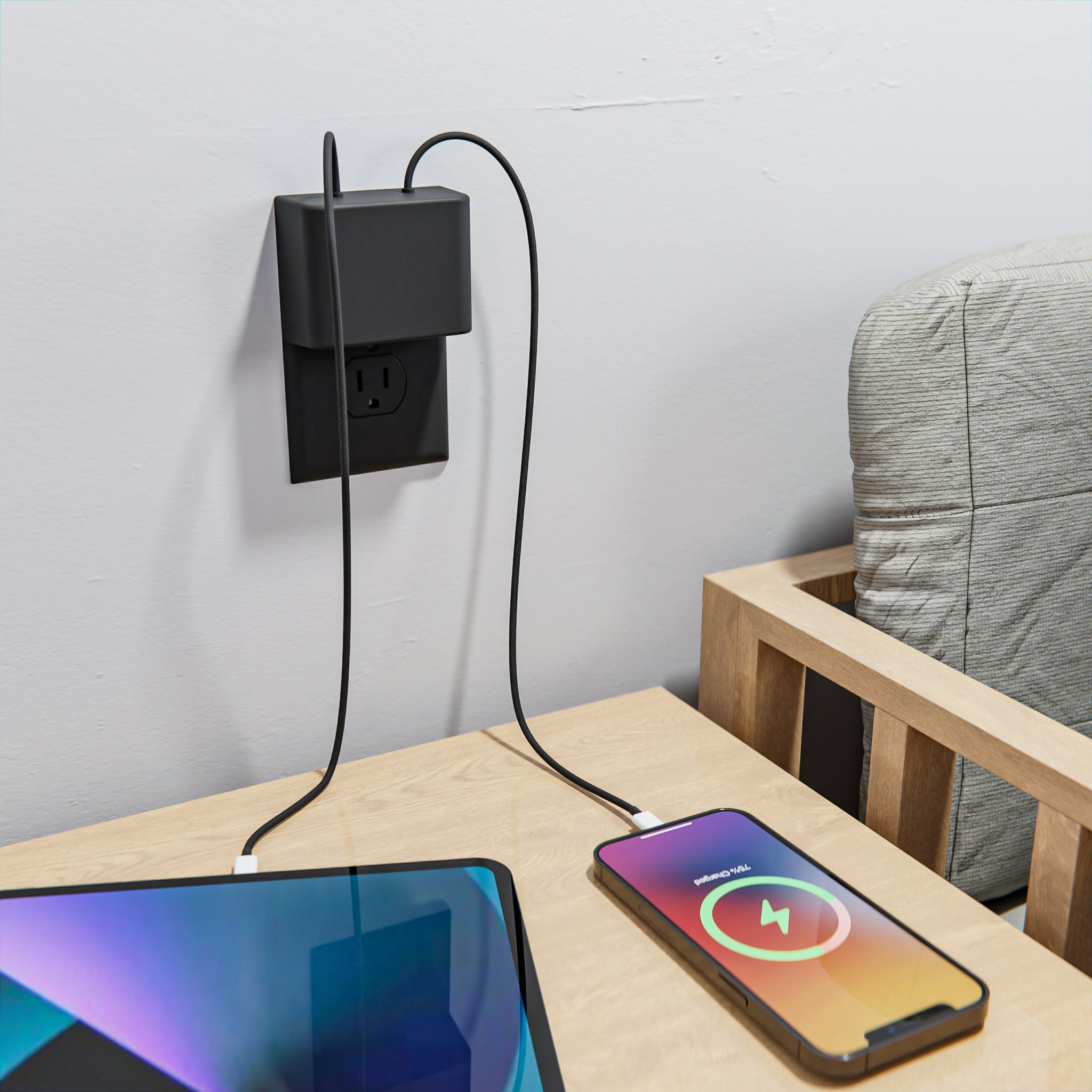 This image features the limited edition black Permaplug Charger Lock Standard model, installed on a standard black outlet in a bedroom setting. A smartphone and tablet are actively charging, with cables connected to the charger lock, which has the central screw hole for standard outlet compatibility. The black charger lock blends seamlessly into the room's minimalist aesthetic, while providing an organized and efficient charging solution for multiple devices.