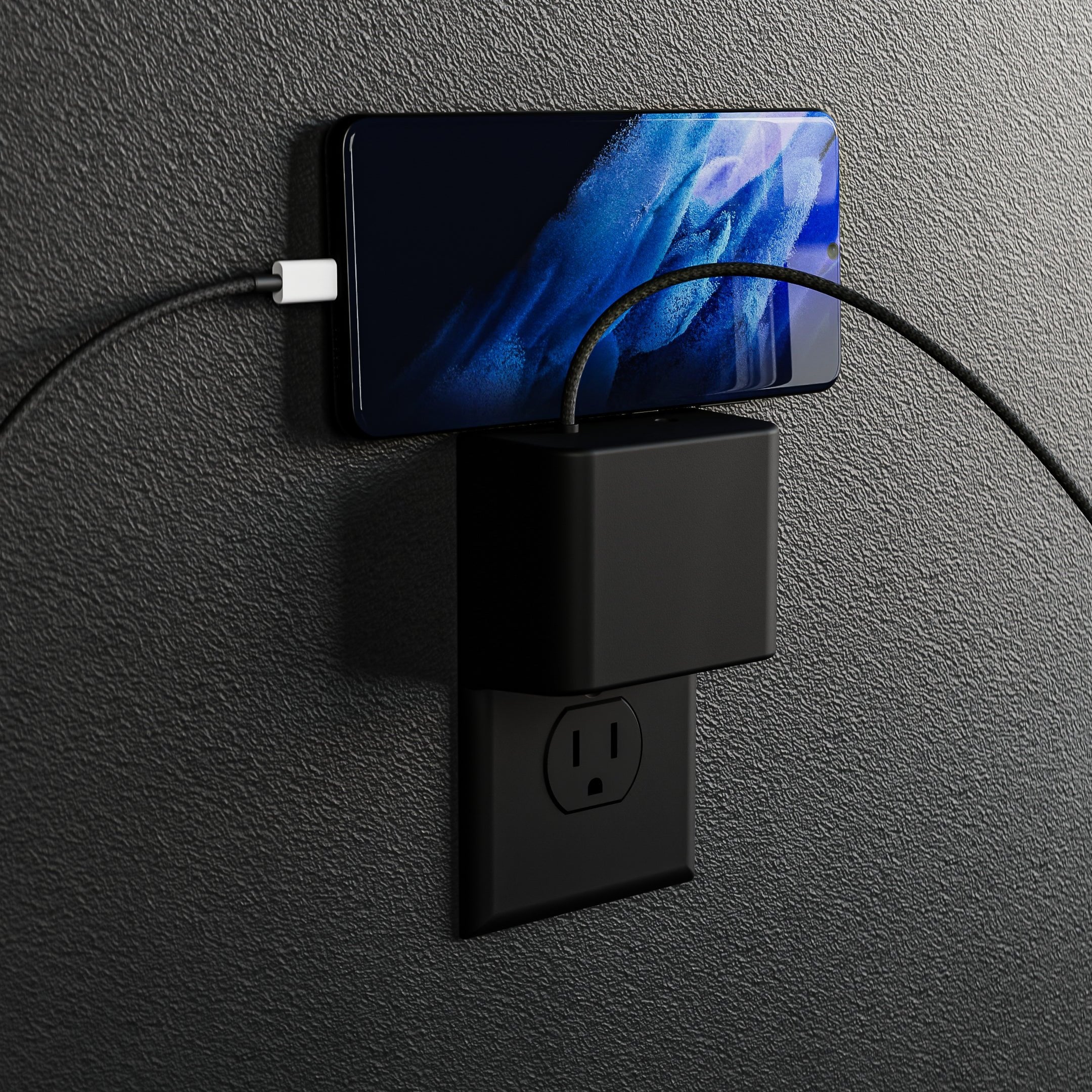 This image features the limited edition black version of the Permaplug Charger Lock Standard model, designed for standard outlets. The distinctive feature of this model is the screw hole located in the center, fitting standard-style outlets. The sleek black finish offers a modern and stylish look, and the setup shows a smartphone charging securely with two cables connected. The black-on-black design enhances the minimalist aesthetic, blending seamlessly into the background while providing an organized and s